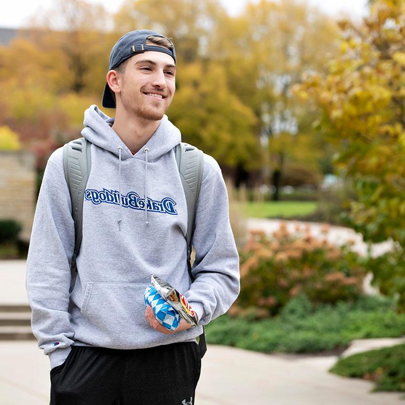 A Drake University student walking outside wearing a backpack holding a single serving bag of chips and a sandwich